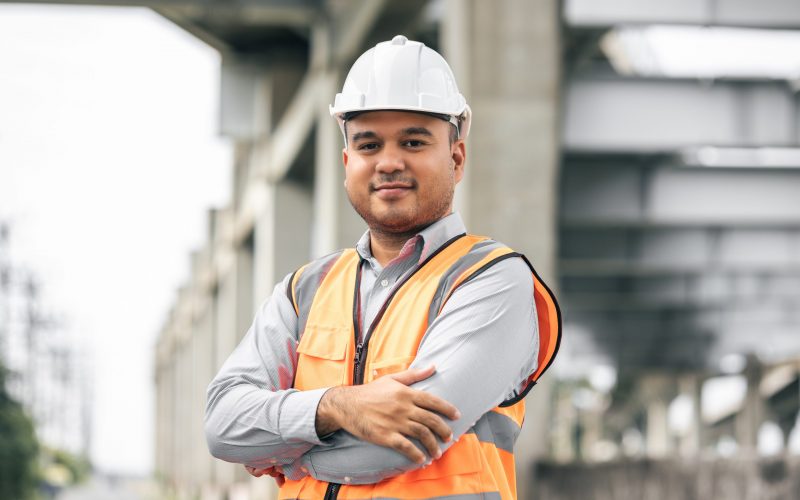 Asian engineer handsome man or architect looking construction with white safety helmet in construction site. Standing at highway concrete road site.